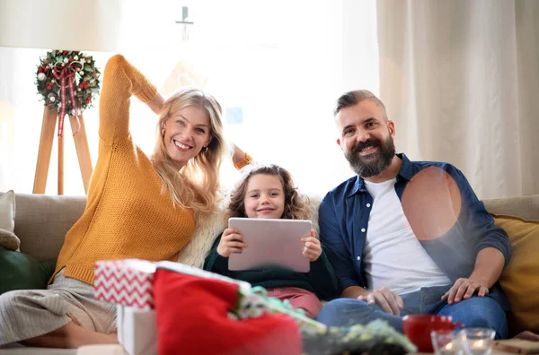 Couple avec petite fille à l'intérieur à la maison à Noël, ayant un appel vidéo. — Photo