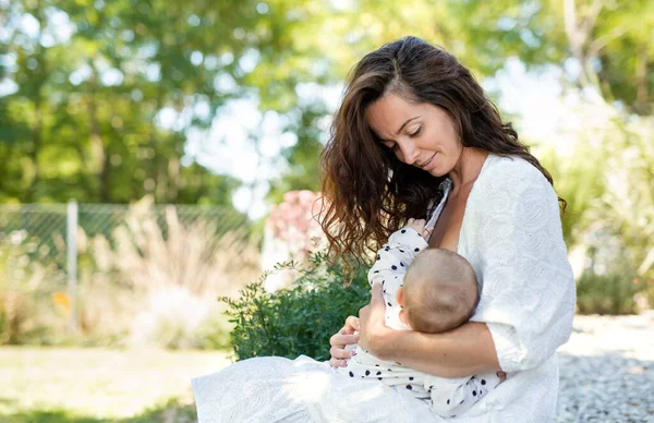 Woman nursing baby girl outdoors in backyard. — Stock Photo, Image