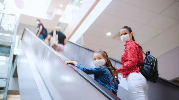 Madre e hija con mascarilla en escalera mecánica en el centro comercial, concepto coronavirus. — Foto de Stock