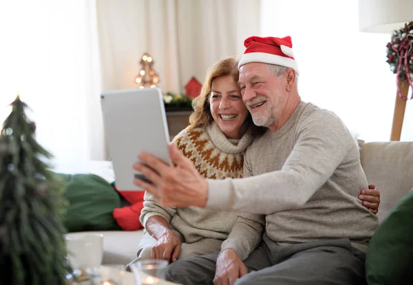 Vue latérale du couple de personnes âgées à l'intérieur à la maison à Noël, ayant un appel vidéo avec la famille. — Photo