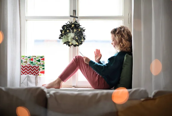 Kleines Mädchen mit Tablet sitzt zu Weihnachten zu Hause und hat Videoanruf. — Stockfoto