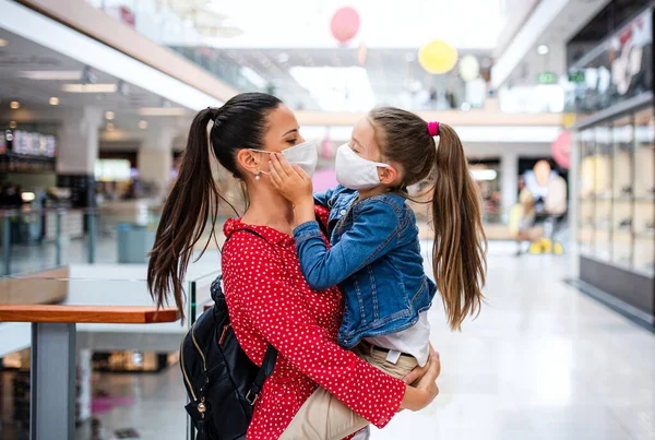 Moeder en dochter met gezichtsmasker staan binnen in winkelcentrum, coronavirus concept. — Stockfoto