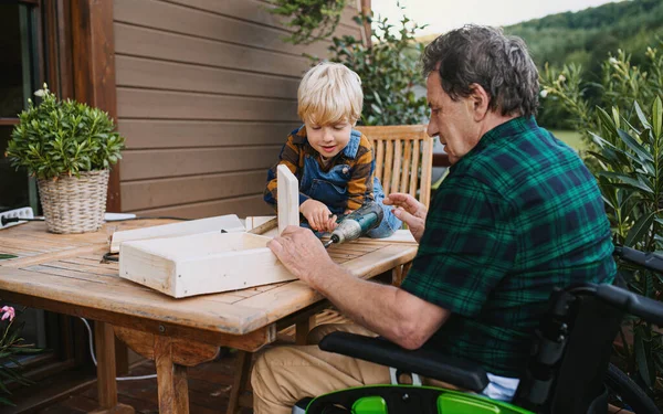 Niño pequeño con abuelo mayor en silla de ruedas construyendo pajarera, proyecto de bricolaje. — Foto de Stock