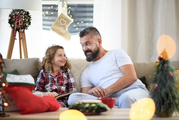Ojciec z małą córeczką w domu na Boże Narodzenie, czyta książkę. — Zdjęcie stockowe