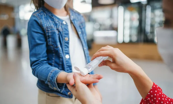 Moeder en dochter met gezichtsmasker desinfecteren handen binnen in winkelcentrum, coronavirus concept. — Stockfoto