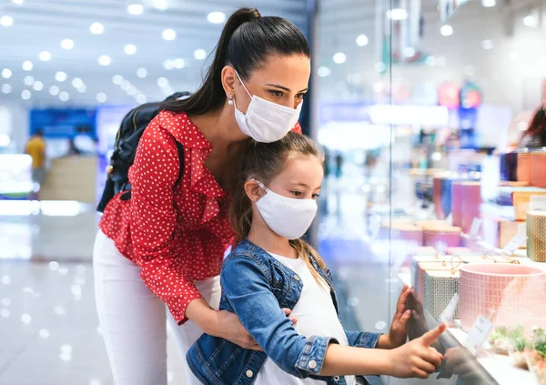 Мати і дочка з маскою для обличчя, що стоїть в приміщенні в торговому центрі, концепція коронавірусу . — стокове фото