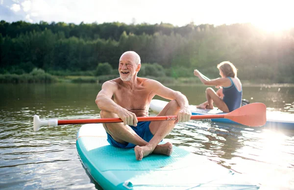 Casal sênior paddleboarding no lago no verão. — Fotografia de Stock