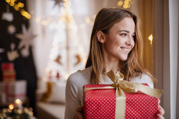 Jovem feliz dentro de casa em casa no Natal, segurando presente. — Fotografia de Stock