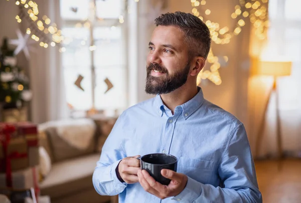 Mature man indoors at home at Christmas, holding cup of tea. — Stock Photo, Image