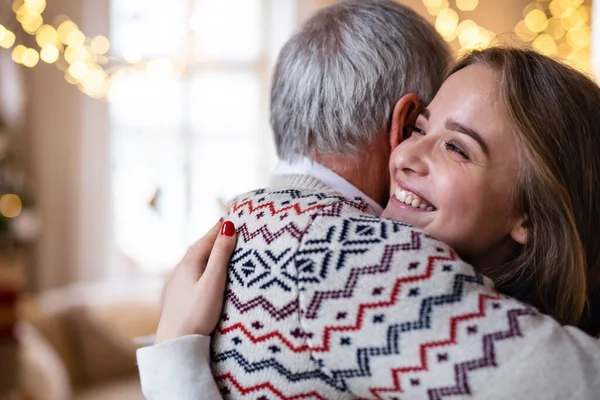Starší muž s mladou ženou doma na Vánoce, objímání. — Stock fotografie