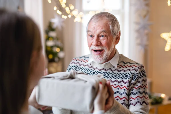 Jonge vrouw geeft cadeau aan verraste grootvader binnen met Kerstmis. — Stockfoto