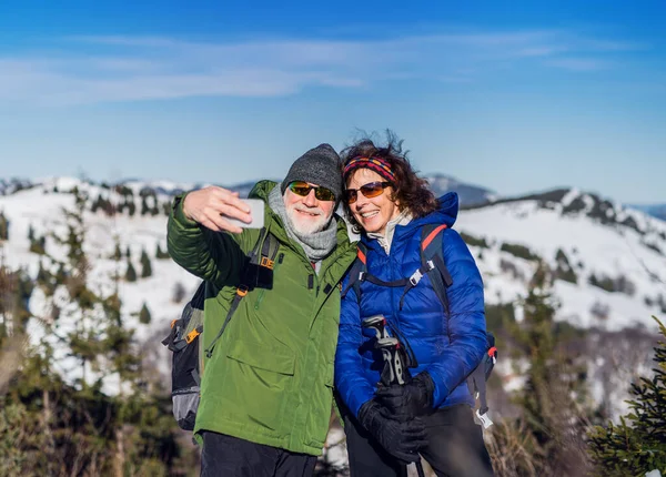 Senioren-Wanderpaar steht in schneebedeckter Winternatur und macht Selfie. — Stockfoto