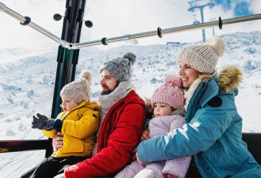 Küçük bir oğlu ve kızı olan bir aile teleferik kulübesinde, karlı kış tatilinde..