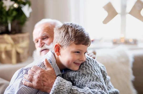 Menino pequeno com avô sênior dentro de casa no Natal, abraçando. — Fotografia de Stock