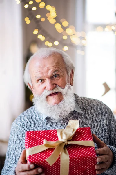 Vue de face de l'homme âgé heureux avec boîte cadeau à l'intérieur à la maison à Noël. — Photo