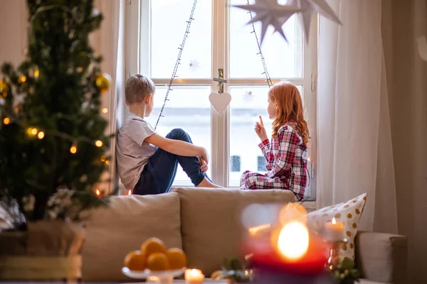 Menina pequena e menino de pijama em casa em casa no Natal, sentado no peitoril da janela. — Fotografia de Stock