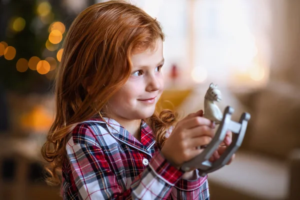 Portret van een klein meisje binnenshuis met Kerstmis, met houten paard. — Stockfoto