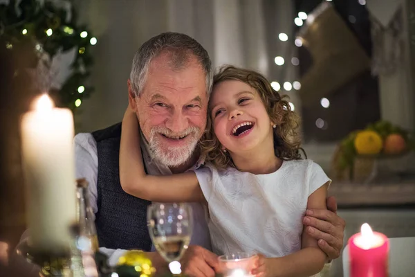 Старший дедушка с маленькой внучкой в помещении на Рождество, сидит за столом. — стоковое фото