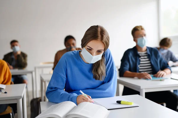 Jóvenes estudiantes con máscaras faciales en los escritorios de la universidad o la universidad, concepto coronavirus. — Foto de Stock