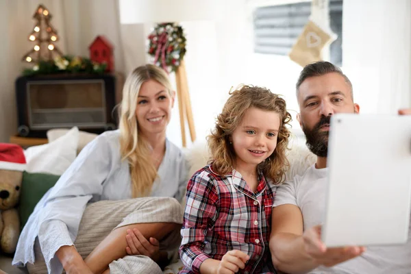 Familj med liten dotter inomhus på julen, med videosamtal. — Stockfoto