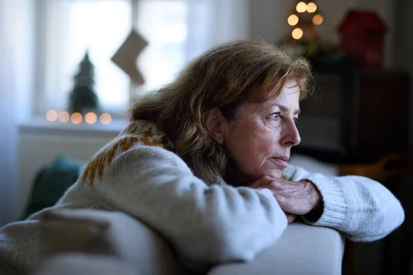 Donna anziana solitaria seduta sul divano in casa a Natale, concetto di solitudine. — Foto Stock