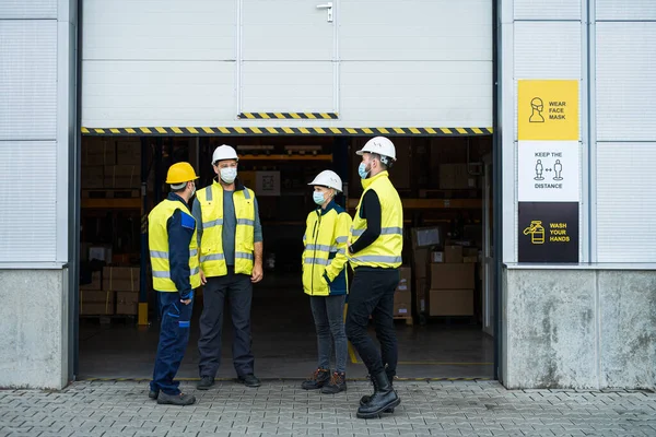 Gruppo di lavoratori con maschera viso parlare davanti al magazzino, concetto di coronavirus. — Foto Stock