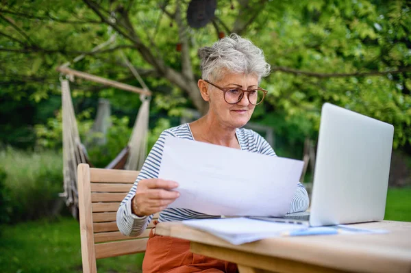 Старша жінка з ноутбуком, що працює за столом на відкритому повітрі в саду, концепція домашнього офісу . — стокове фото