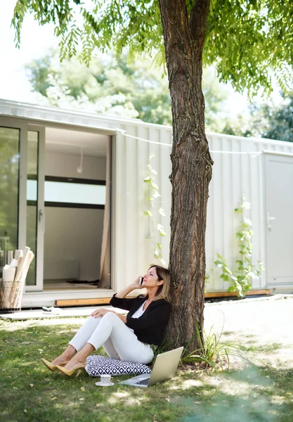 Femme mûre travaillant dans le bureau à domicile en plein air dans le jardin, à l'aide d'un ordinateur portable et smartphone. — Photo