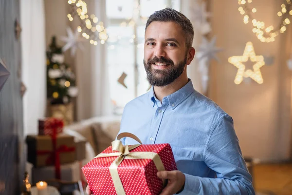 Mature man indoors at home at Christmas, holding present. — Stock Photo, Image