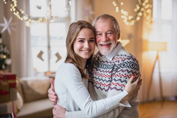 Homem sênior com jovem mulher em casa em casa no Natal, abraçando. — Fotografia de Stock