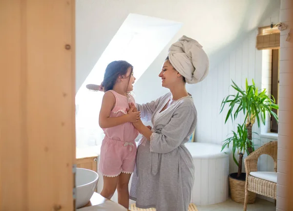 Portrait of pregnant woman with small daughter indoors in bathroom at home, brushing hair. — Stock Photo, Image