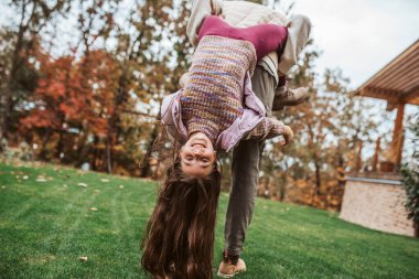 Baba kızıyla oynuyor, onu sonbahar bahçesinde baş aşağı tutuyor..