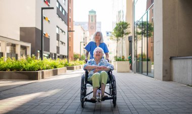 Tekerlekli sandalyedeki yaşlı kadın, bakıcı asistanıyla temiz havanın tadını çıkarıyor..