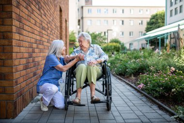 Tekerlekli sandalyedeki kıdemli hasta, kadın bakıcısıyla konuşuyor..