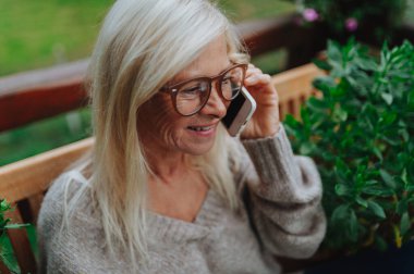 Son sınıf öğrencisi terasta durup telefonla konuşuyor ve gülümsüyor..