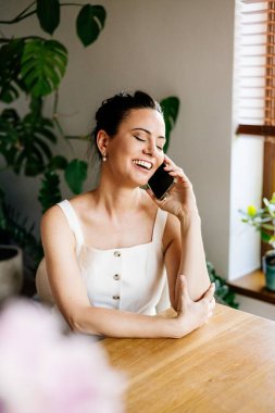 Kendine güveni tam bir kadın koltukta oturuyor ve evde huzurlu bir şekilde telefonla konuşuyor..