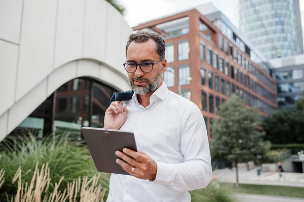 Modern ofis binasının önünde elinde tablet olan ve bir şeyler okuyan bir iş adamı..