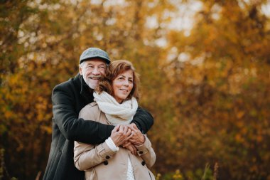 Yaşlı çift sonbahar mevsiminde, sonbahar yapraklarıyla çevrili olarak dışarıda vakit geçiriyorlar..