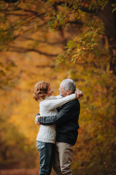 Older couple spending time outdoors in fall season, surrounded by autumn leaves.