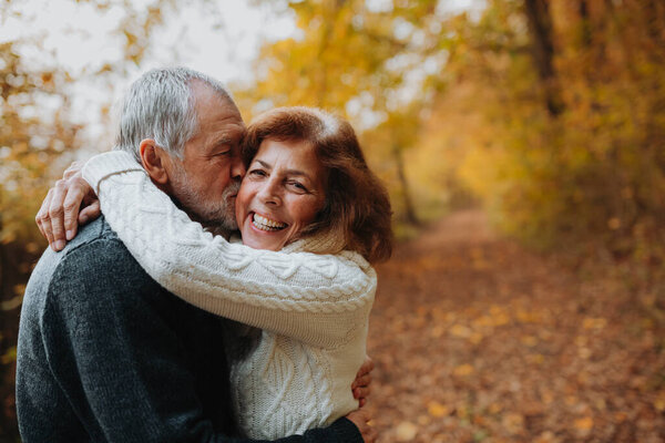 Older couple spending time outdoors in fall season, surrounded by autumn leaves.