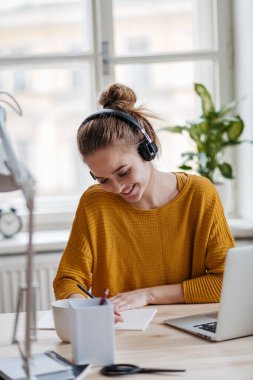 Kulaklıklı bayan öğrenci masada oturuyor ve ders çalışıyor..