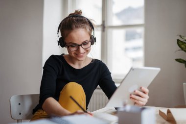 Kulaklıklı bayan öğrenci masada oturuyor ve ders çalışıyor..