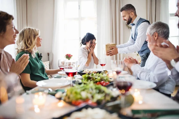 Un Homme Offrant Un Cadeau A Une Jeune Femme Surprise Lors D Une Fete D Anniversaire De Famille Repas Aine Stock Photo