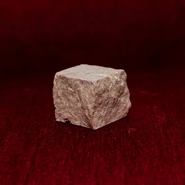Rough stone cube isolated on blurred red background; focus on stone