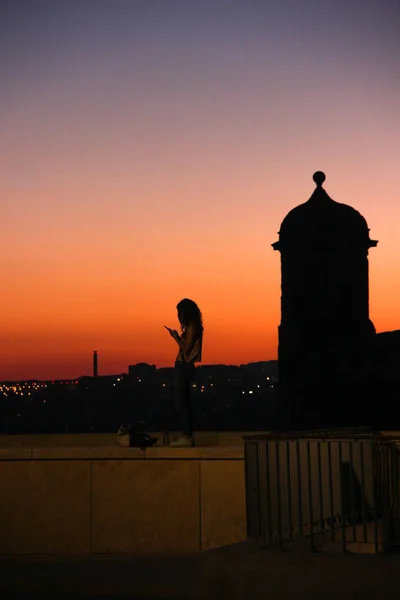 Genç kadın surf cep telefonu arka plan parlayan günbatımı üzerinde