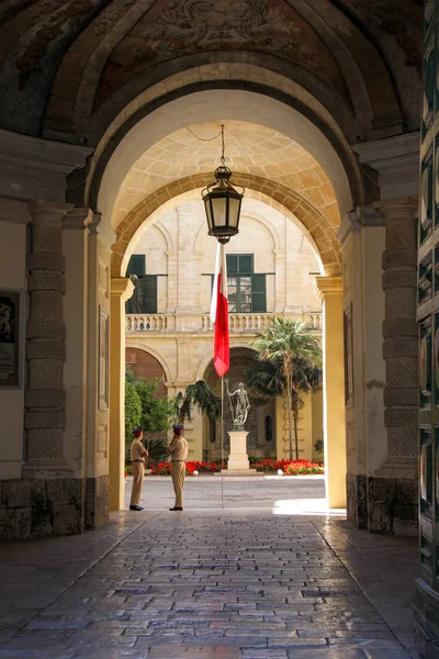 Visa från arch hänrycka av Grandmaster Palace innergård med maltesisk flagg och två soldat i Valletta — Stockfoto