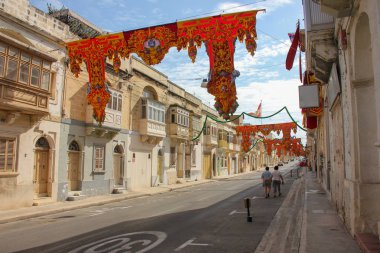 Eski geleneksel balkonlu neredeyse boş festively dekore edilmiş sokak. İki yetişkin Marsa, Malta güneşli bir günde yıllık festa dini tatil için afiş altında yürüyüş