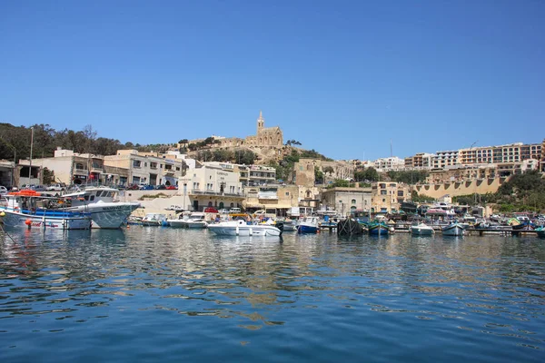 Mgarr, Malta - Mayıs 2018: Gozo Feribot Terminali'ne görünümü Mgarr. Kilise üstünde belgili tanımlık tepe üzerinde arka plan ile ön plan ve eski şehir yatlar ile defne. Mavi su yansımalar