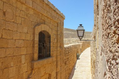 Güneşli günde mavi gökyüzü altında fenerle antik sarı boş sokak daraltmak için eski şehir içinde pencere görünümünden oda. Victoria, Gozo, Malta