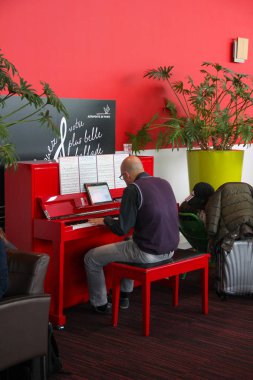 Paris, France - april 2016: Bald man in glasses playing the red piano at an airport lounge Charles de Gaulle Airport clipart